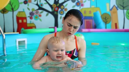 Woman shows a yellow ball to a kid in the swimming pool.