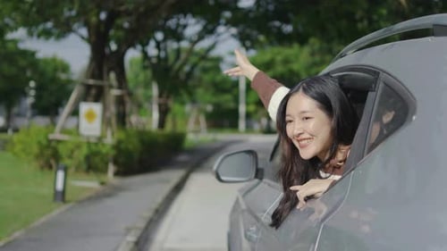 Happy cute young woman enjoying sitting in car watching a beautiful sunset tree view, hand greeting