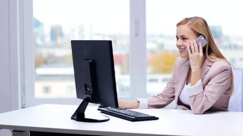 Lächelnde Geschäftsfrau im Büro, die Smartphone und Computer zur Kommunikation nutzt