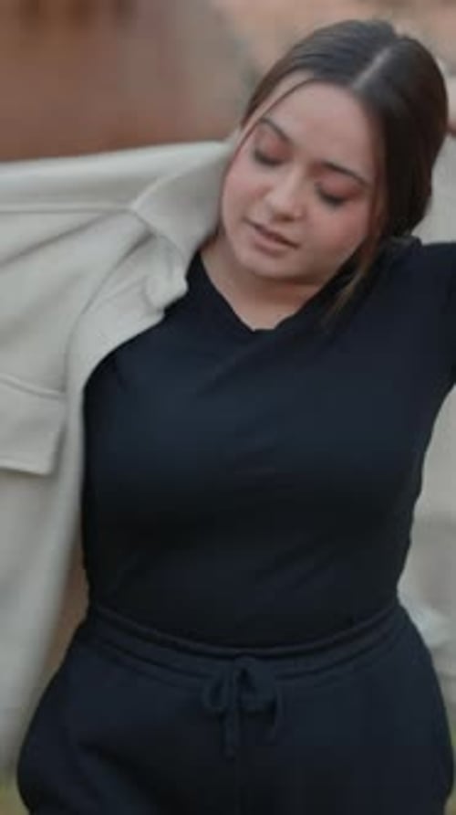 Young Woman Putting On Jacket Outdoors