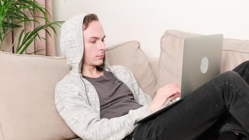 Young Adult Lies on Couch Typing on Laptop