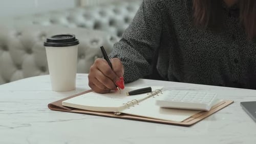 Woman Writing in Notebook at Desk with Coffee