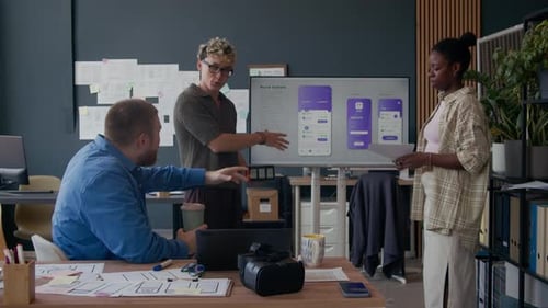 Asiatischer Mann diskutiert mit Kollegen, die im Büro präsentieren, über das UI-Design für mobile App