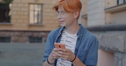 Slow Motion of Cheerful Asian Man Using Smartphone Touching Screen and Smiling in City Street