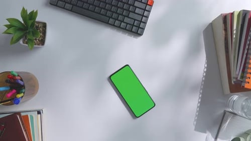 Top down view of a mock up green screen smartphone on a white office desk