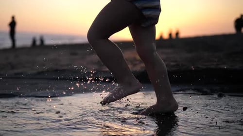 Slow Motion Footage of a Small Barelegged Child Running Along the Edge of the Shore Ankledeep in