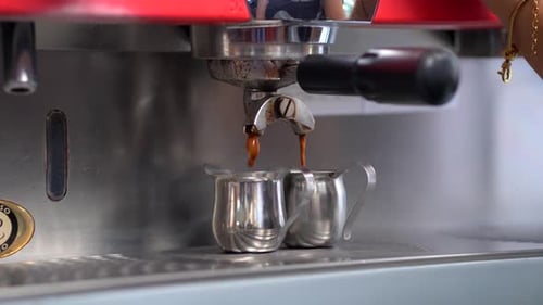 Cafeteria making a preparation of espresso or American coffee from a machine in stainless steel cups