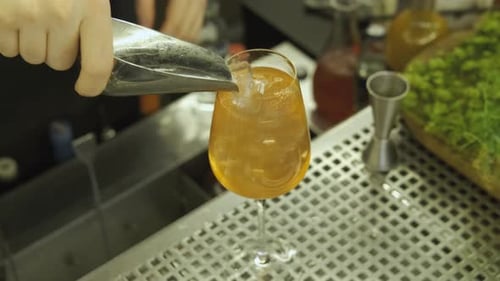 close-up bartender puts ice into a glass with a cocktail