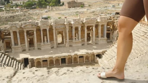 A view of women's legs walking on the top rows of the ancient, ruined amphitheater, the ruins of Hie