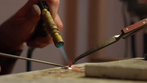 Handwerker lötet Metallteile in einer Werkstatt bei Tageslicht mit einer Fackel