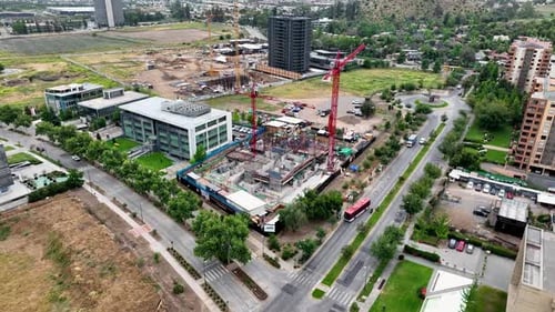 Drone aerial of construction site with red cranes, foundation work, busy street intersection, and