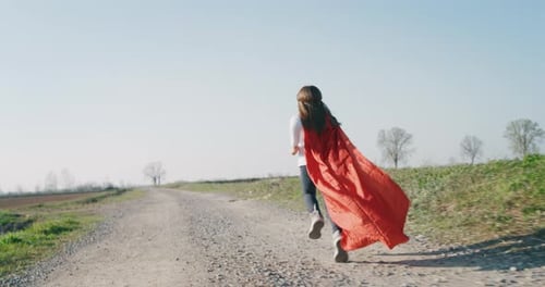 Authentic shot of a funny little girl dressed as superhero in red cape running and having fun on a