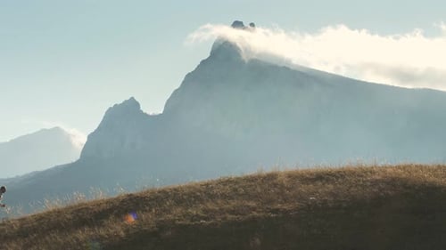 A Runner Strenuously Runs Along the Top of the Holna Against the Backdrop of a Picturesque Mountain