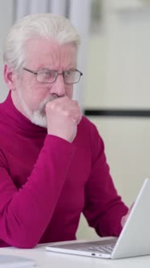Senior Man Coughing While Using Laptop Indoors