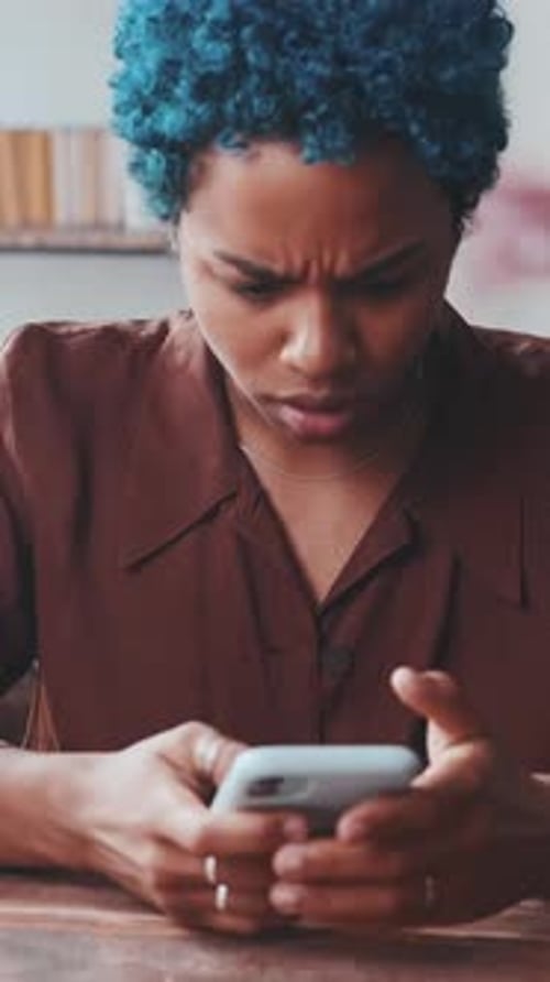 Young Puzzled African American Woman Upset Reading SMS on Phone Sits at Table