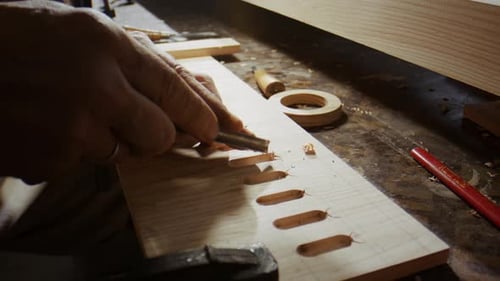 Man chiseling wood in workshop with hand tools