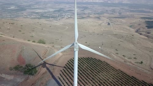 Aerial footage of Wind turbines spinning, in a mountain forest surrounding