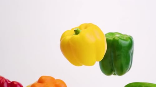 Colorful medley of red, orange, yellow and green bell peppers raining down and bouncing off each oth
