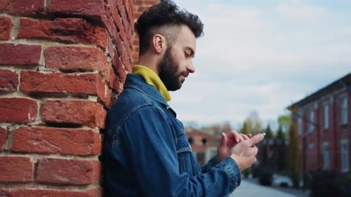 Young Man Using Smartphone Leaning on Brick Wall