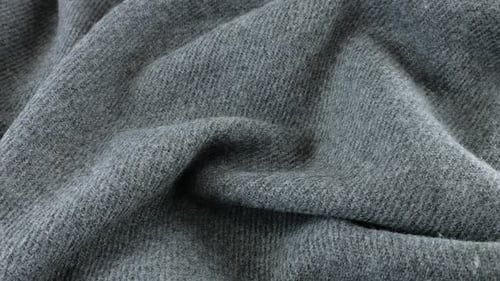 Top view of the soft folds of textured gray wool fabric rotated on the display case.