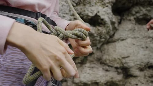 A Female Rock Climber Ties a Climbing Knot to a Harness Before Climbing a Steep Cliff