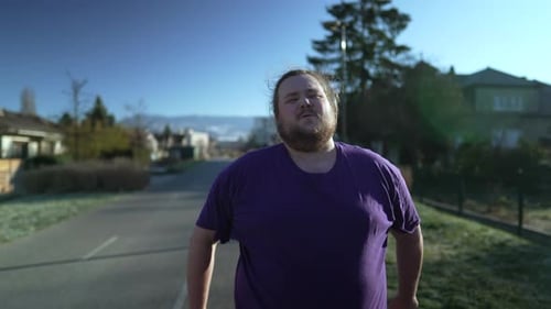 One angry overweight man walking outside. An upset young pensive person walks in street
