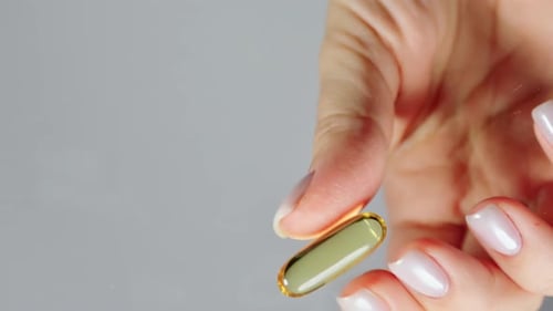 Woman's fingers take one capsule of fish oil from a transparent surface
