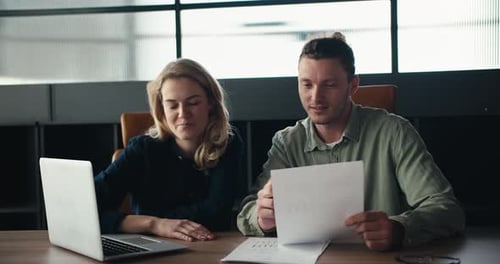 Colleagues Collaborate Using Laptop and Documents in Office