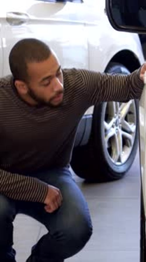 Thoughtful Man Inspects Car Wheel at Modern Dealership