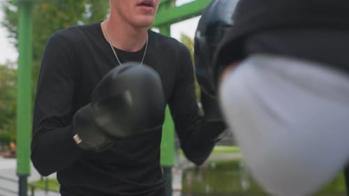 Athletic Men Training Outdoors with Boxing Gloves and Pads