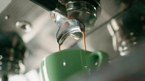 Pouring coffee flows from the machine into the cup making hot drink using the filter holder freshly