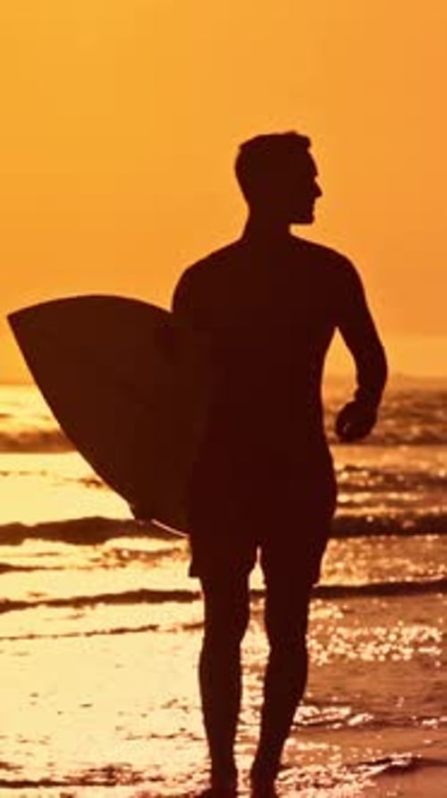 Surfista caminhando na praia ao pôr do sol