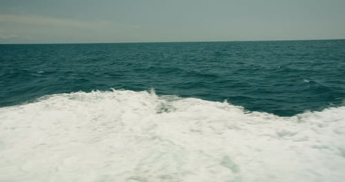 The boat wake creates a frothy texture on the blue Mediterranean waters. A white foam path stretches