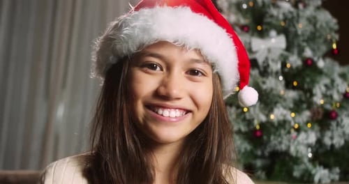 Smiling Girl with Santa Hat near Christmas Tree