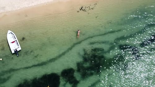 Descend aerial drone shot of woman lying in crystal clear ocean on sunny day