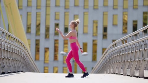 Young fit woman in pink sportswear works out on bridge, wide side view