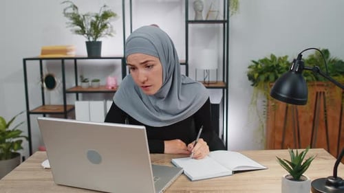 Muslim Business Woman Study with Notebook at Home Office on Laptop Computer Talking to Webcam Online