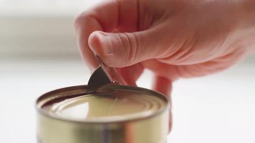 Man opening a can of tomato sauce with a can opener. Close up