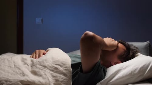 Man Suffering From Insomnia Covering Ears with Hands While Trying to Sleep