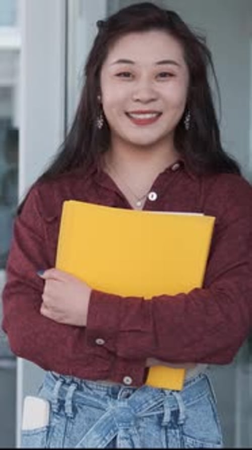 Female University Student Holding Folders and Looking at the Camera While Standing at the Hallway