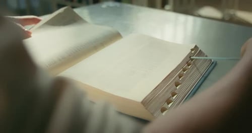 Woman Reads a Book Sitting on a Chair in a Library and Bookmarks One of the Pages