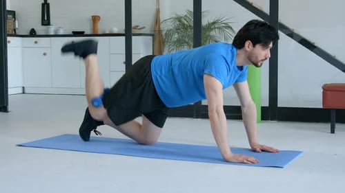 Motivated Sporty Fit Man Exercising Donkey Kick with Dumbbell Indoors