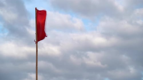 Red flag waves dramatically in a cloudy sky
