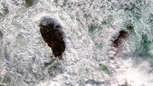 Slow motion, aerial shot of powerful waves with white caps crashing on a set of sea rocks and colour