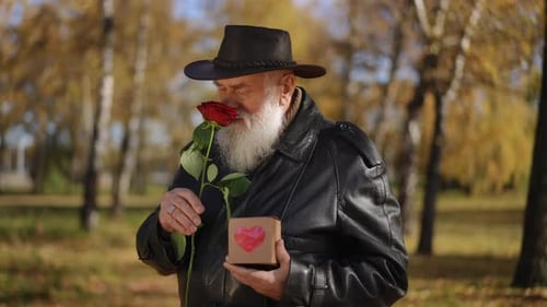 An Elderly Man Holding a Rose and a Thoughtful Gift While Enjoying the Autumn Park Scenery