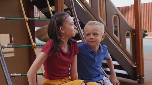Closeup of Two Children Sitting on a Rope Ladder on the Playground and Laughing