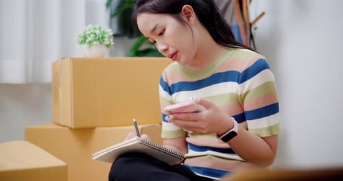 Woman with Phone and Notebook by Cardboard Boxes