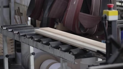 Slow motion close-up of wood on a conveyor belt coming off a wood working machine.