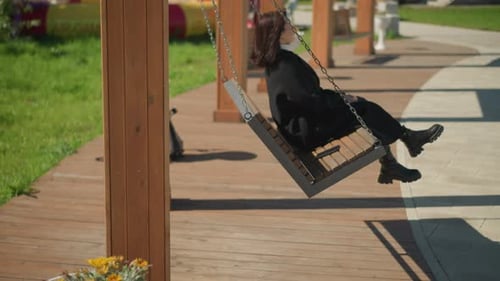 Vue latérale d'une dame élégante se relaxant sur une balançoire dans un parc animé