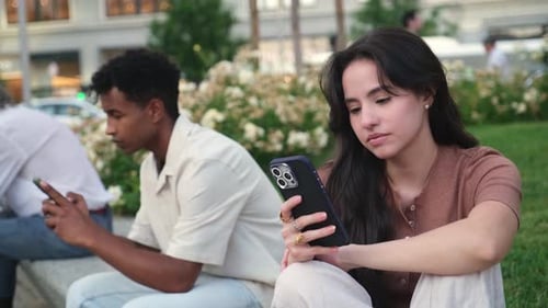 Young woman using smartphone next to a man in a park